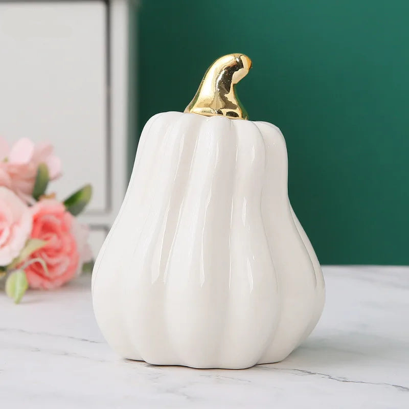 White ceramic pumpkin with gold top on a light surface with flowers in the background